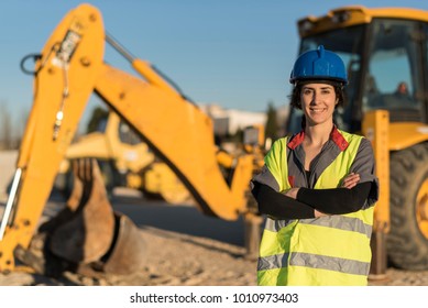 Posing woman looking at camera with hardhat and excavator shovel in background