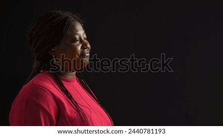 Positioned against isolated black backdrop young woman wears downcast facial expression. Side-view portrait of african american fashion blogger in a mournful stance against blank background.