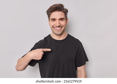 Positiver erwachsener Mann zeigt sich lächelnd zu nahe legt, dass seine Hilfe prachtvolles Lächeln auf Gesicht gekleidet in lockeren schwarzen T-Shirt sich selbstwichtig einzeln auf weißem Hintergrund. Das bin ich.