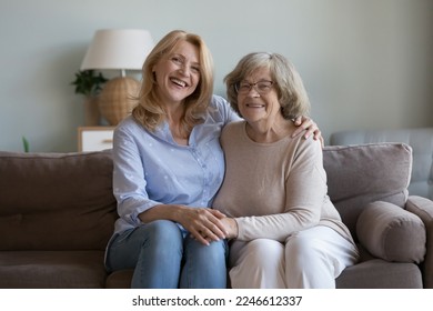 Positive adult mature daughter woman and elderly mother sitting on home sofa together, hugging with affection, holding hands, smiling at camera, laughing, enjoying meeting, family leisure time - Powered by Shutterstock