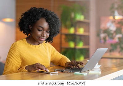 Positive african american businesswoman using mobile phone, working with laptop in cafe, copy space
