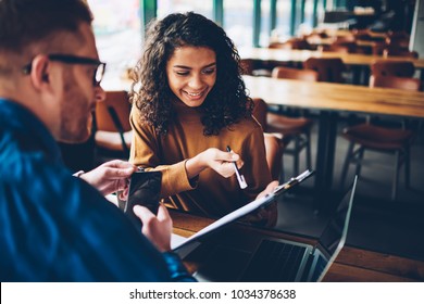 Positive african american student with curly hair showing own design project to colleague studying in university.Happy dark skinned young woman reading working plan sitting together with friend - Powered by Shutterstock