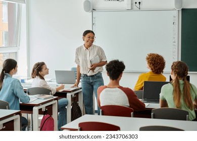 Positive african american teacher with notebook standing near pupils and devices in classroom - Powered by Shutterstock