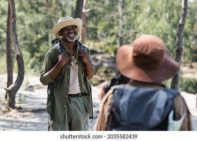 Positive african american traveler looking at blurred wife in hat in forest - Powered by Shutterstock