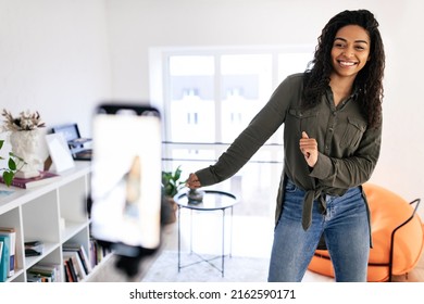 Positive African American Young Lady Filming Video Blog For Social Network, Using Cell Phone On Tripod To Broadcast Her Dance In Living Room, Selective Focus On Youth Person. Content Creator Concept