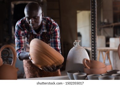 Positive African Potter Enjoying Work, Checking Ceramic Products In Pottery Studio