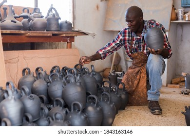 Positive African Potter Enjoying Work, Checking Ceramic Products In Pottery Studio