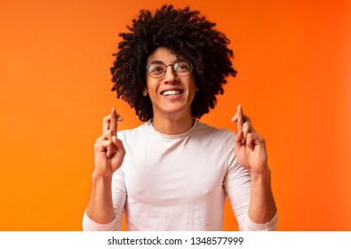 Positive african-american guy crossing fingers, making wish, hopes for fortune and good luck, orange background