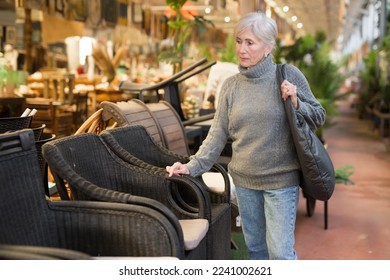 Positive aged female shopper choosing resin wicker chairs for using in outdoor patio or garden in furnishing salon .. - Powered by Shutterstock