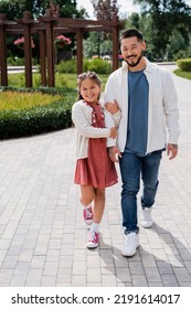 Positive Asian Girl Holding Hand Of Dad While Walking In Summer Park