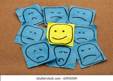 positive attitude or optimism concept - happy smiley face on yellow sticky note surrounded by sad unhappy blue faces