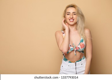 Positive attractive blonde young model wears swimsuit and white skirt being happy to receive good news. Joyful woman rejoices weekends, relaxing indoors, isolated against beige background.