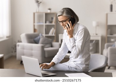 Positive attractive businesswoman leads pleasant business, personal conversation on smartphone, using laptop discuss deal detail with customer or colleague, provide professional consultation distantly - Powered by Shutterstock