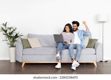 Positive attractive interracial young couple middle eastern man and indian woman using computer at home, cheerful spouses planning weekend or vacation, booking cheap tickets on Internet, copy space - Powered by Shutterstock