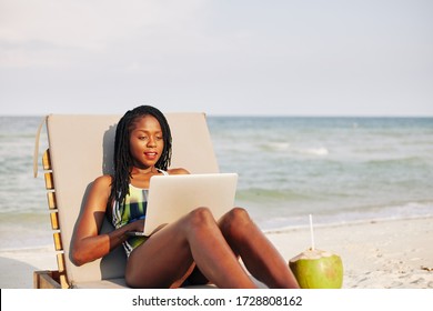 Positive Attractive Young Black Woman Resting On Chaise-lounge And Watching Tv Series On Laptop Screen