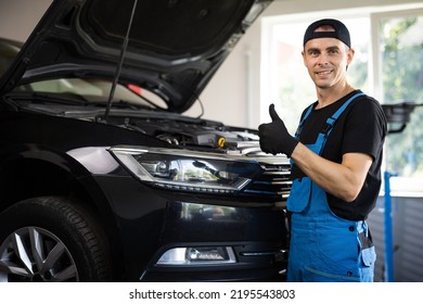 Positive auto service worker smiling to camera and showing thumb up gesture, approving car repair workshop. Portrait of car mechanic in a car workshop shows thumbs up, in the background of service. - Powered by Shutterstock