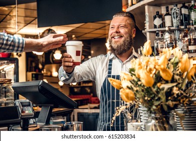 Positive bearded barista male selling coffee to a consumer in a coffee shop. - Powered by Shutterstock