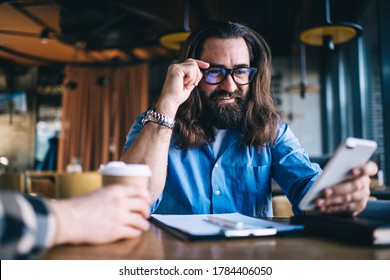 Positive Bearded Caucasian Male Using Mobile Phone For Checking Banking Account Owning Small Business, Smiling Mature Man In Spectacles For Vision Correction Satisfied With Getting Good News Via Mail