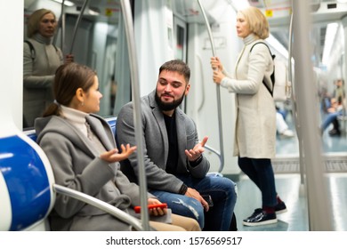 Positive bearded guy enjoying friendly conversation with young woman while traveling on subway train