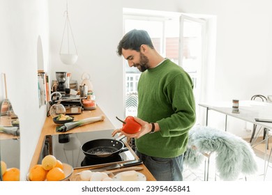 positive bearded man holding bell pepper near frying pan while cooking breakfast at home - Shutterstock ID 2395465841