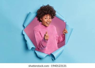 Positive Beautiful Curly Ethnic Woman Makes You Got This Gesture Praises Good Job Points At You Encourages Person Smiles Gladfully Wears Knitted Sweater Breaks Through Blue Paper Background.