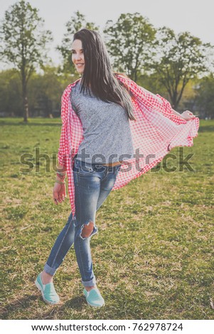positive beautiful hipster woman in park. Looking at camera. Positive human emotion facial expression body language, concept of funny girl. Dressed in a gray t-shirt, blue ripped jeans