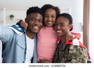 Positive black family father, daughter and mother soldier posing with flag of the US, african american woman in military uniform return home from army, celebrating reunion with husband and kid