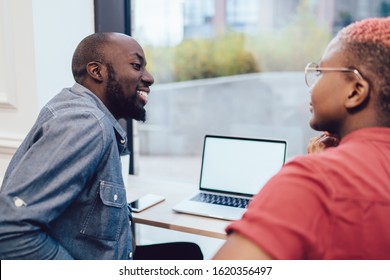 Positive Black Guy In Casual Clothes Creating Startup Using Laptop Discussing Strategy With African American Crop Lady In Office Looking At Each Other