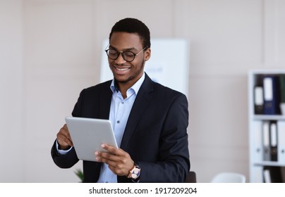 Positive Black Guy Young Entrepreneur Using Digital Tablet In Office, Copy Space. Smiling African American Manager Checking His Agenda On Pad, Enjoying Modern Technologies For Business