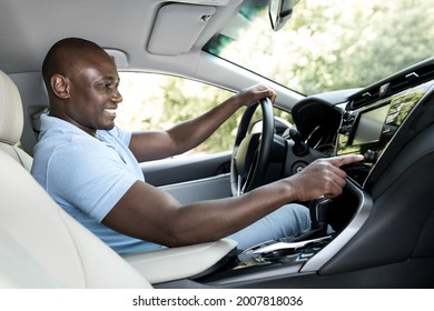 Positive Black Man Sitting At Brand New Car Front Seat, Making Test Drive, Turning Music On, Checking Automobile Stereo System, Side View, Copy Space. Happy African American Driver Going To Job