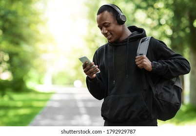 Positive Black Man With Wireless Headset Using Mobile Phone, Coming Back From Training At Park, Empty Space