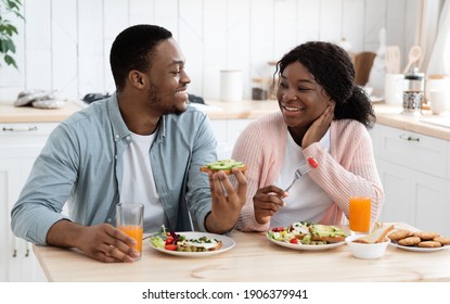 Positive Black Spouses Eating Tasty Breakfast And Drinking Orange Juice In Kitchen, Happy African American Man And Woman Sitting At Table Chatting And Smiling, Enjoying Spending Time At Home