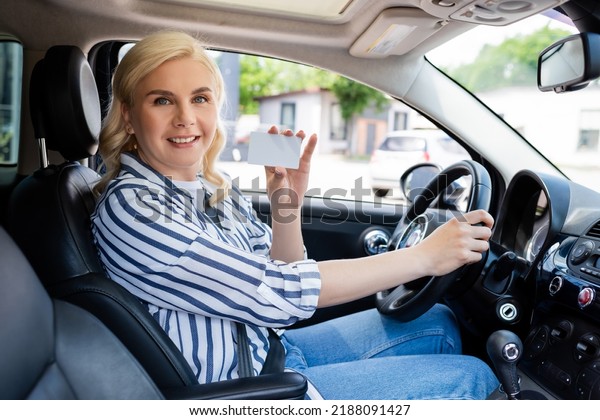 Positive blonde\
driver holding license in\
auto