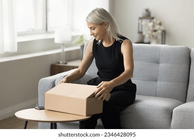 Positive blonde senior woman packing parcel for sending. Retired customer opening paper container, getting cardboard package, cargo from transportation delivery courier service - Powered by Shutterstock