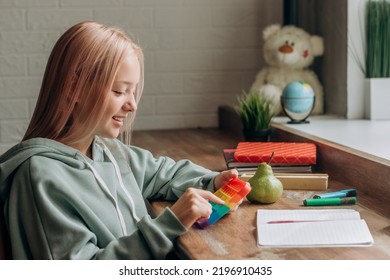 Positive Blonde Teenage Girl Playing With Colorful  Toy While Studying At Home.Trendy Anxiety And Stress Relief Fidgeting Game.School Concept.