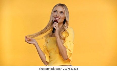 Positive Blonde Woman Singing Karaoke And Touching Hair Isolated On Yellow