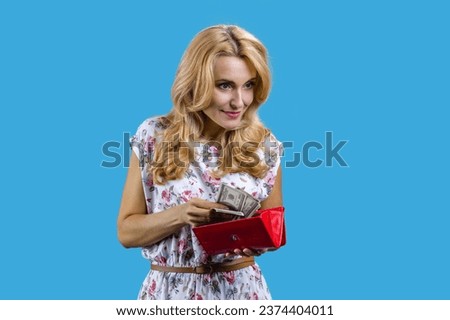 Positive blonde woman taking money from her wallet. Isolated on blue.