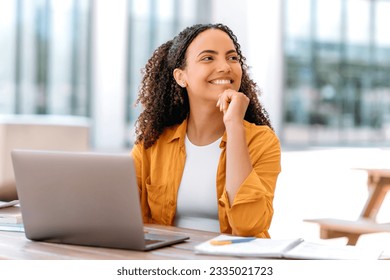 Positive brazilian or hispanic curly haired girl, freelancer, female student, IT specialist, sit outdoors, with laptop, looks happily to the side, thinking about something good, dreaming, smiling - Powered by Shutterstock