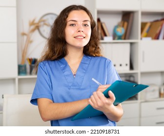 Positive Brown-haired Nurse Woman Standing And Writing Medical History Sheet In Medical Center