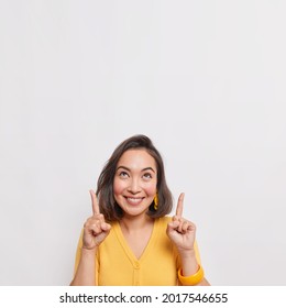 Positive brunette Asian woman points above shows place for your advertising text smiles pleasantly wears yellow jumper earrings and bracelet isolated over white background. Great idea cool offer - Shutterstock ID 2017546655