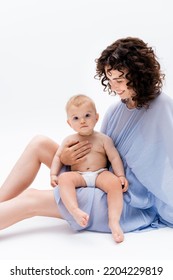 Positive Brunette Mom Looking At Baby Daughter While Sitting On White Background