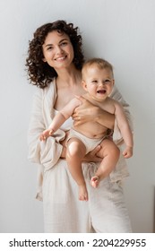 Positive Brunette Mom In Pajamas Holding Baby Girl At Home