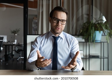 Positive business professional in suit and glasses looking and speaking at webcam during video call, virtual conference. Businessman, teacher, coach giving workshop, webinar. Head shot portrait