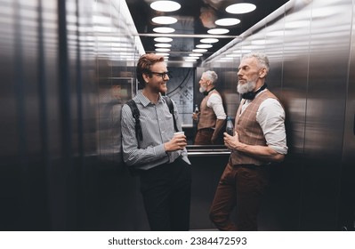 Positive businessman talking with elderly colleague by modern elevator