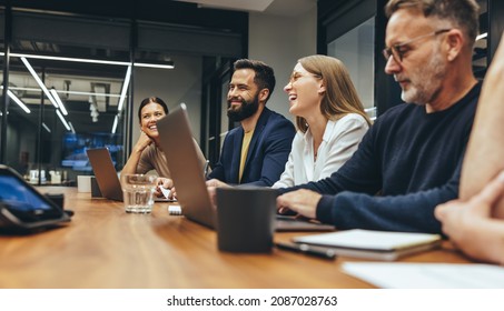 Positive businesspeople having a meeting in a boardroom. Group of happy businesspeople smiling while working together in a modern workplace. Diverse business colleagues collaborating on a project. - Powered by Shutterstock