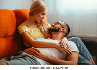 Positive Caucasian Couple Bonding On An Orange Couch At Home, Looking At Each Other, Deeply In Love.Grain Effect.