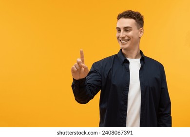 Positive caucasian guy touching invisible screen and smiling, copy space on yellow studio background. Happy young man pushing button on virtual display, interacting with touchscreen - Powered by Shutterstock