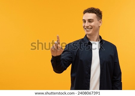 Positive caucasian guy touching invisible screen and smiling, copy space on yellow studio background. Happy young man pushing button on virtual display, interacting with touchscreen