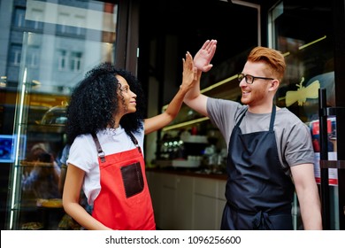 Positive caucasian waiter and cheerful african american waitress in aprons working in team and giving five each other for great job in common cafeteria standing outdoors.Partnership concept - Powered by Shutterstock