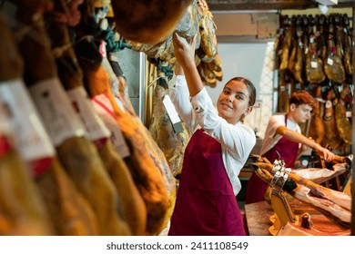 Positive caucasian woman spanish jamon seller arranging dry-cured pig's legs on showcase. - Powered by Shutterstock